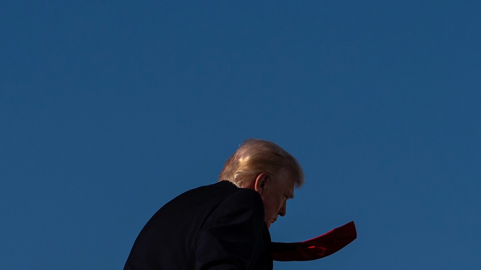 Trump walks away from the camera, showing half his profile and his red tie flapping