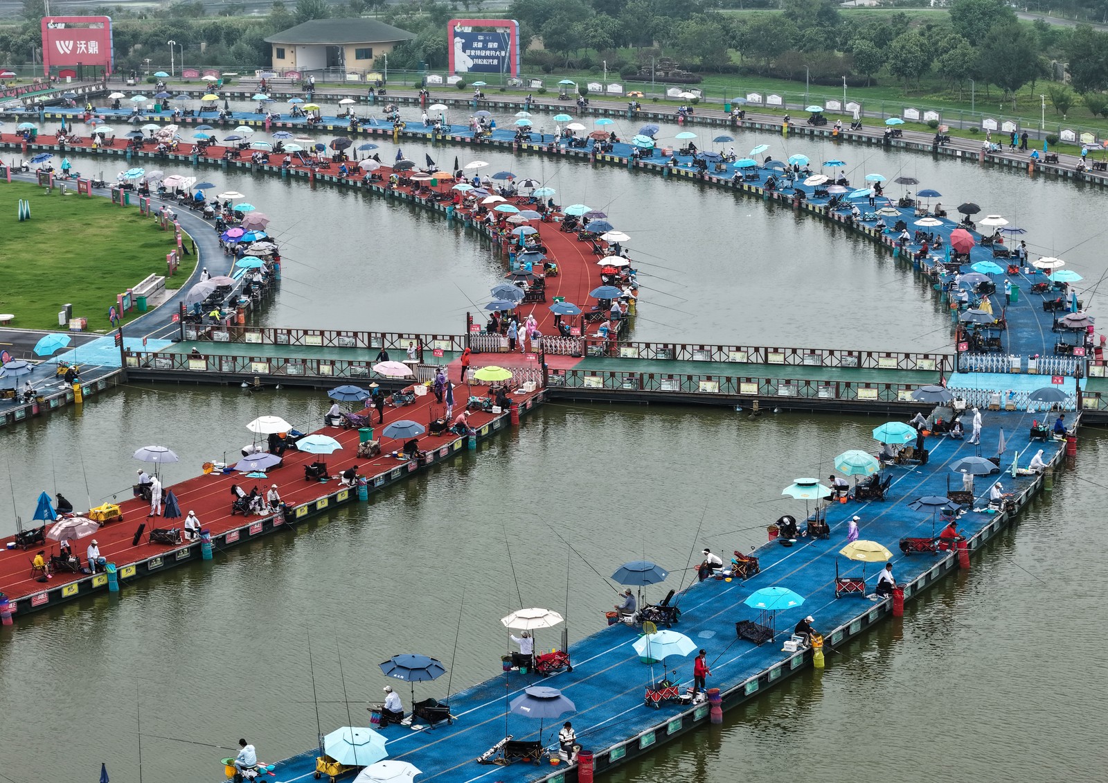 Dozens of people sit on chairs along circular walkways, competing in a fishing contest.