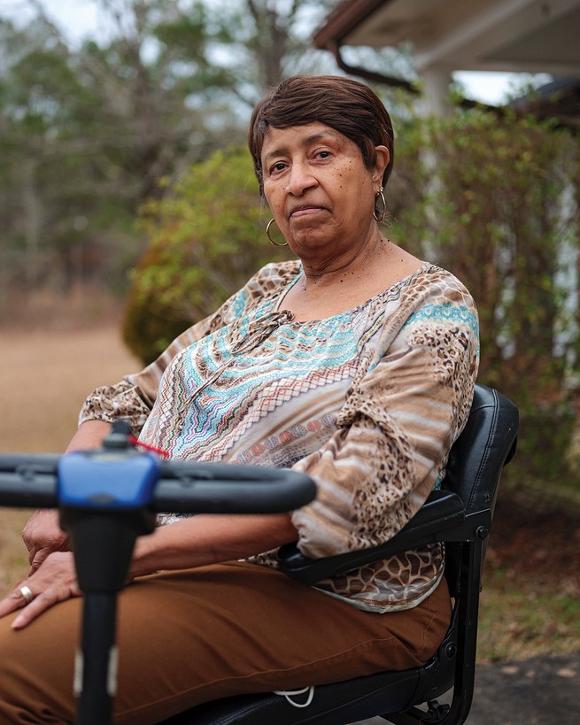 photo of woman sitting in mobility device with porch and yard in background