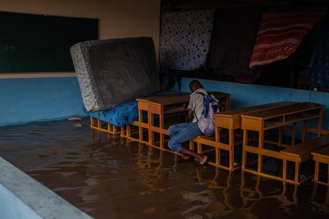 A child sits in a flooded classroom, next to mattresses set up to dry, as heavy rainfall brought by Tropical Storm Grace flooded the area on August 17, 2021, in Les Cayes.