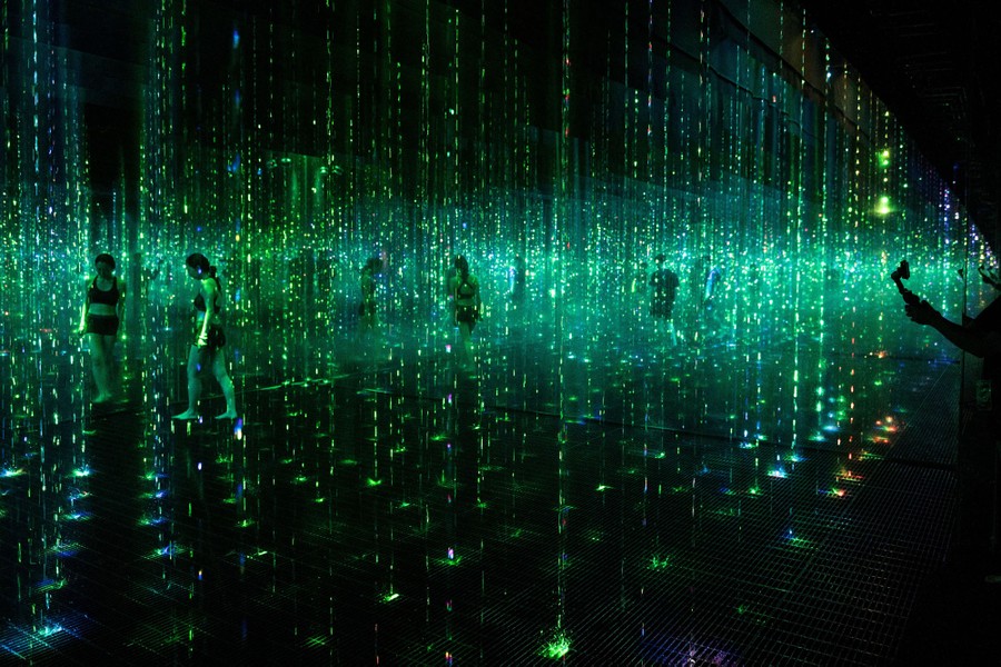 People walk in a dark room filled with illuminated water jets.