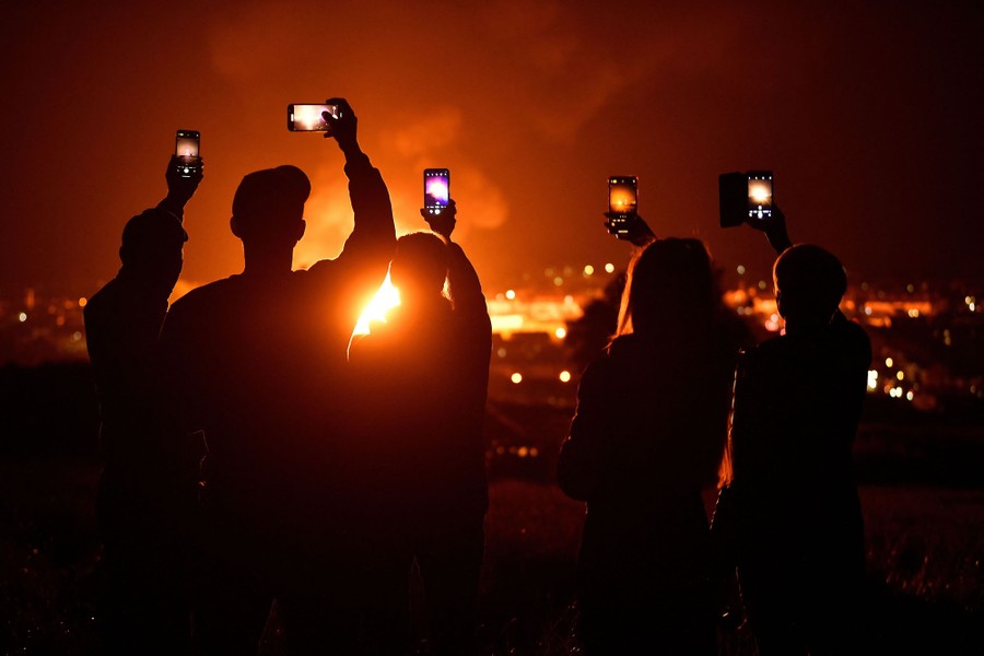 People hold up pones to take photos and video of a large bonfire.