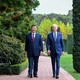 Xi Jinping and Joe Biden, both wearing blue suits, walking side by side on a brick path through a garden