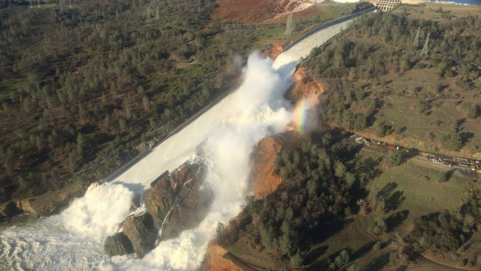 Water pours over the damaged main spillway at the Oroville Dam and over a hillside.