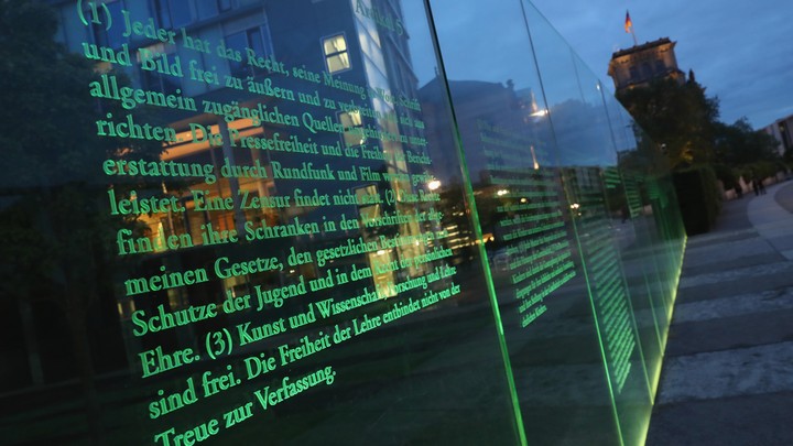 Articles of Germany's Basic Law (Grundgesetz), including article 5, which guarantees freedom of expression, the arts, and the press, stand illuminated on a glass wall in Berlin.