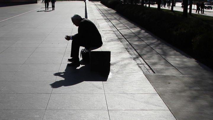 The silhouette of a man looking at his phone as he sits on a long bench
