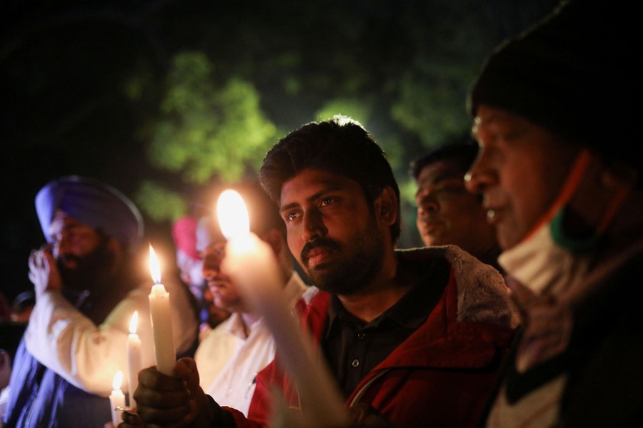 About half a dozen people stand together holding candles during a vigil.