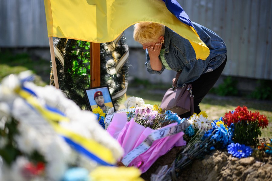 A woman holds a hand to her face as she leans over flowers on the grave of her son.