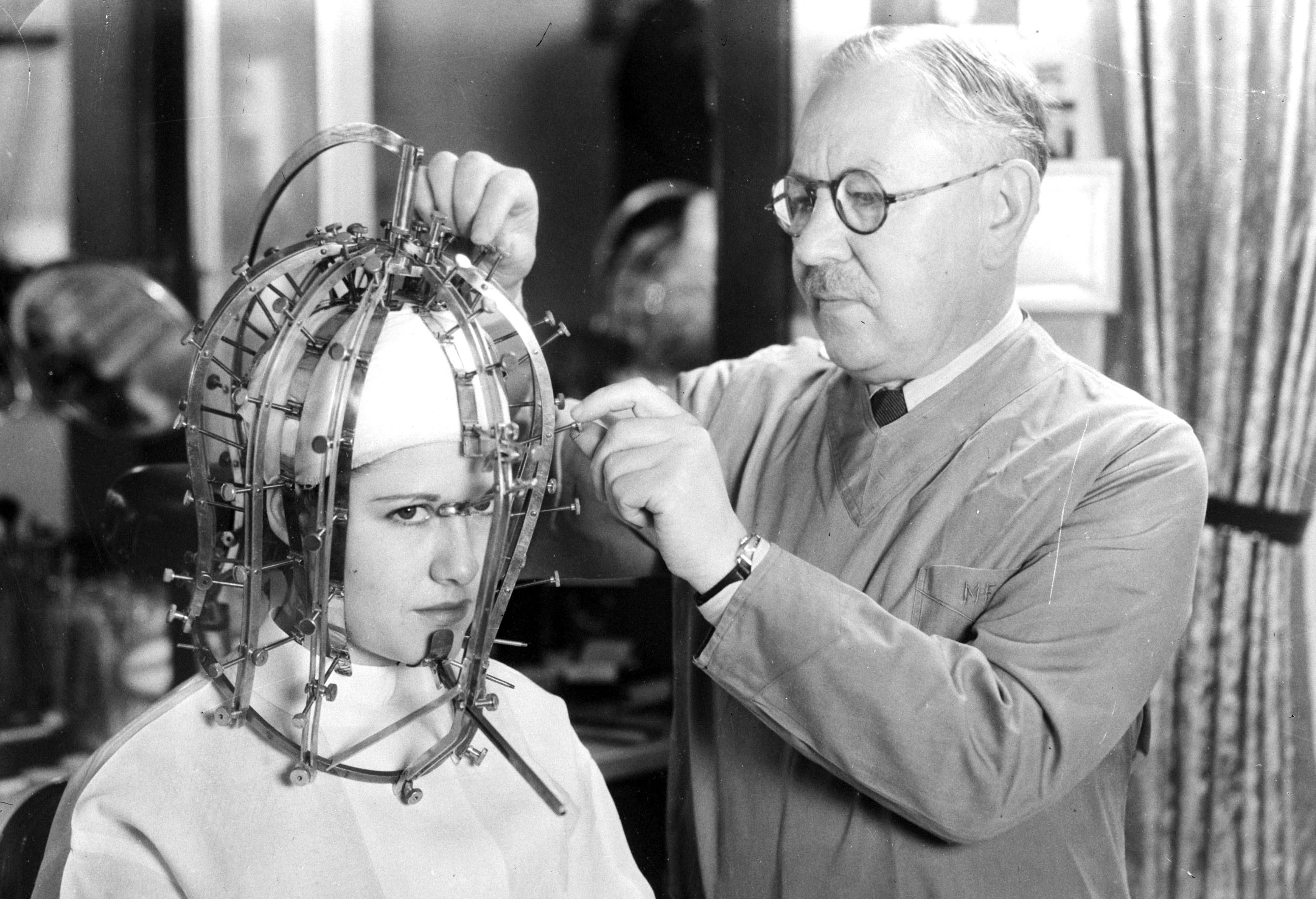 A man uses a strange contraption to measure the size and shape of a woman's head.