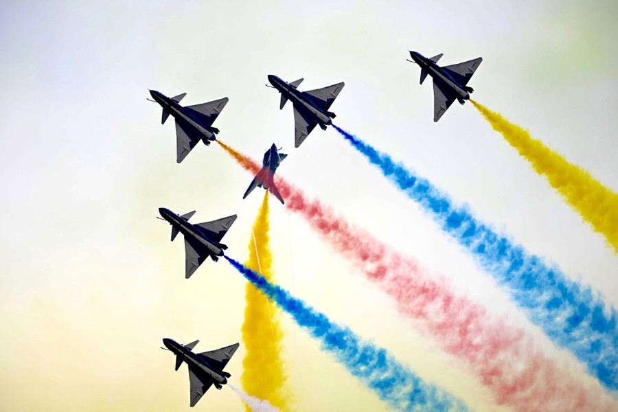 Six planes fly in formation, trailing colorful smoke trails.