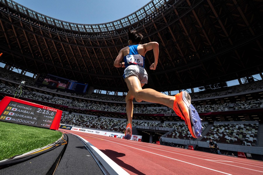 A person runs on a track inside a large, empty stadium.