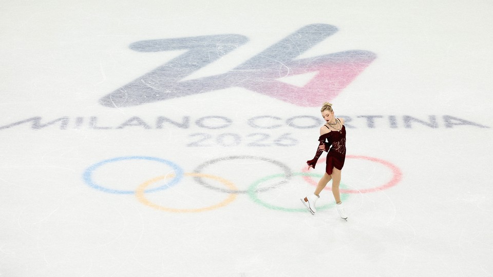 Photograph of Amber Glenn in a red dress ice skating over the logo for the 2026 Olympics