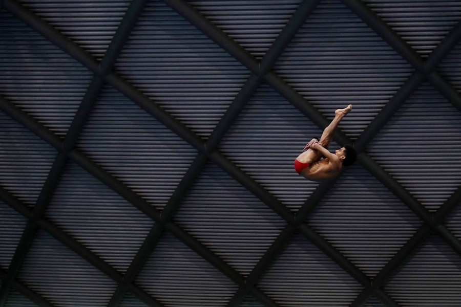 A diver holds his legs to his body as he turns through the air during a high dive.