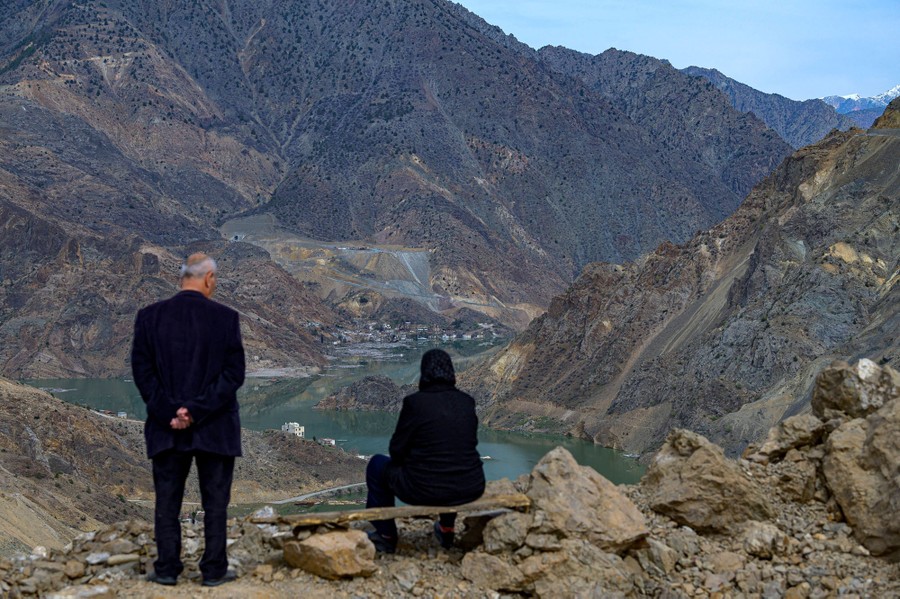 Two people on a rocky ridge look down into a valley that is flooding.