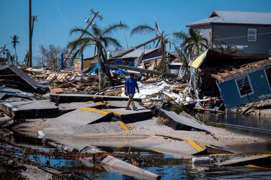 A person walks across a badly broken-up road, surrounded by storm debris.