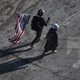 two people walk on snowy ground, one holding an American flag on his shoulder