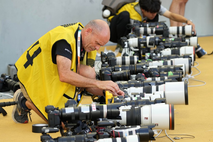 Photographers work on two remote cameras that sit among many other cameras with long lenses, on the ground along a track.