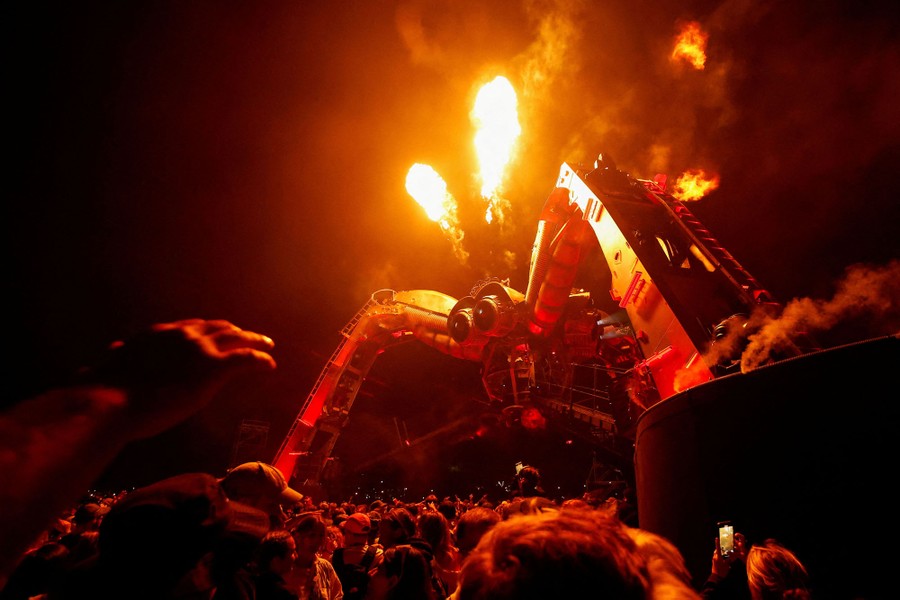 A crowd gathers beneath a spider-shaped sculpture that spouts fire into the air.