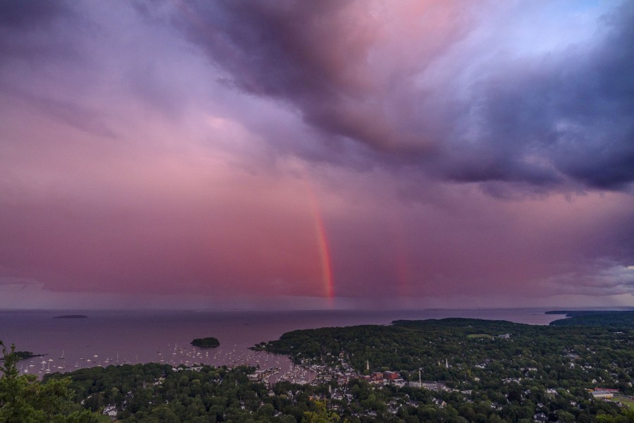An elevated view of a rainbow over a harbor, near a small Maine town.