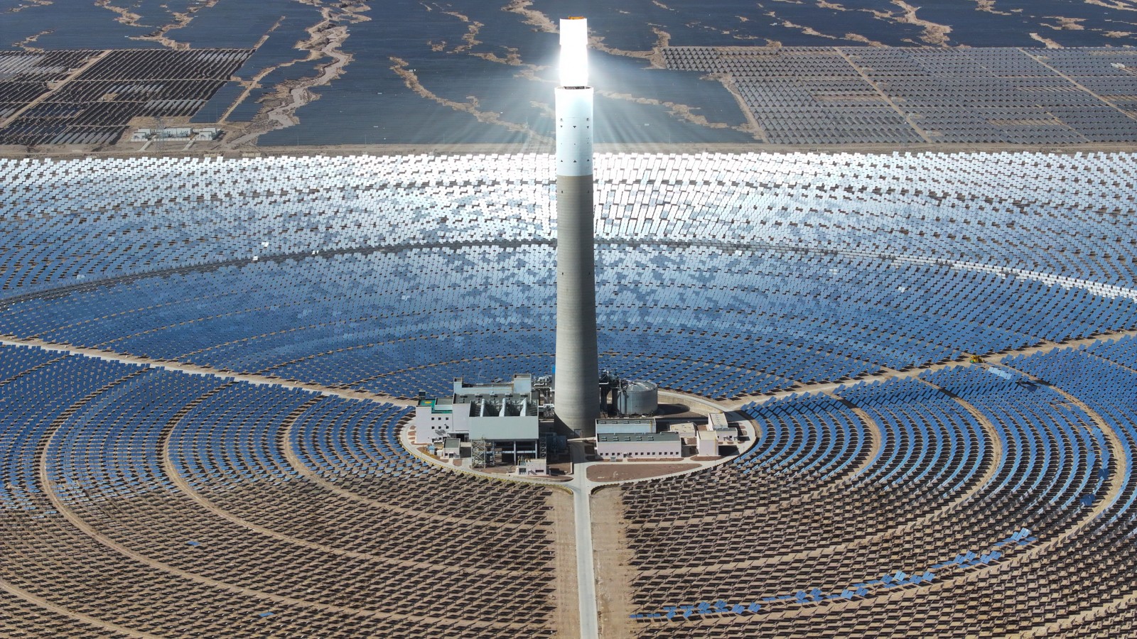 An aerial view of a solar thermal plant—a tall cylindrical column being illuminated by sunlight reflected from a huge array of large mirrors arranged in concentric circles around its base