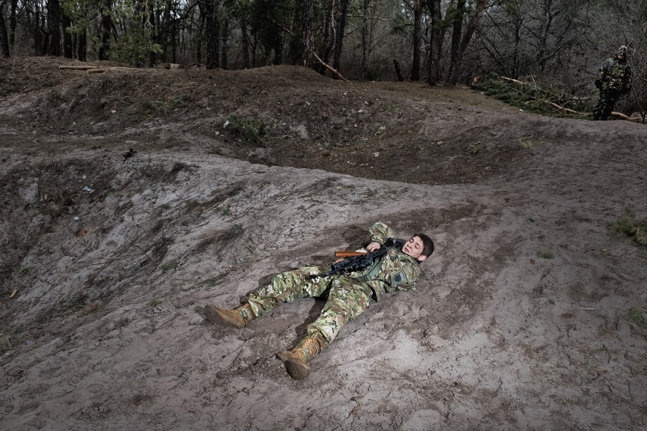 a young man lays down on a hill and aims his gun