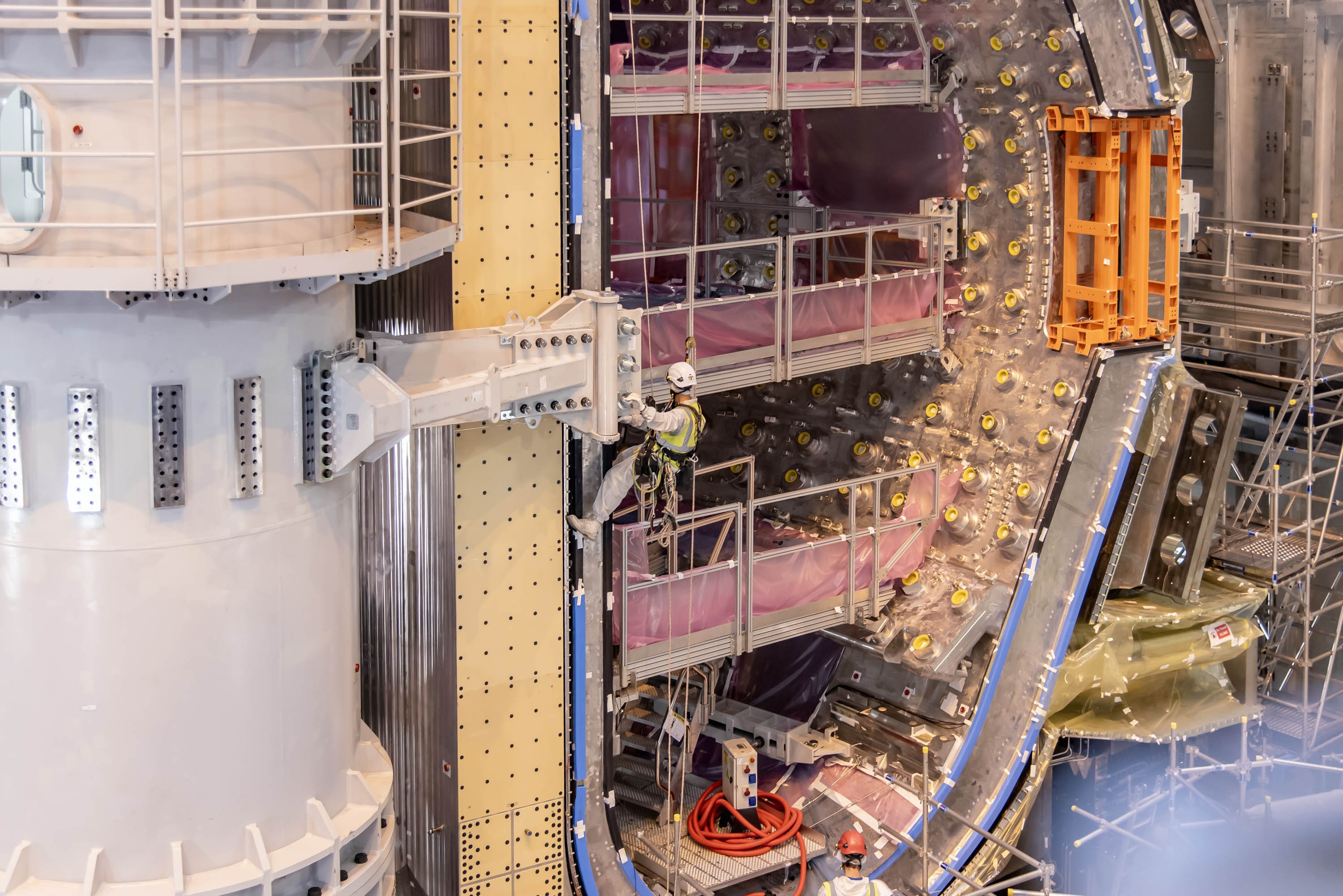 A worker rappels down the side of a large component of a fusion reactor that is under construction.