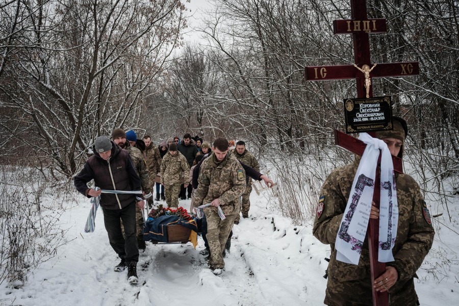 People carry a coffin on a snow-covered trail through a forest.