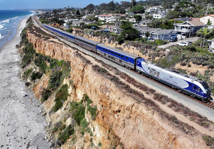 An aerial view of a train passing along eroding cliffs above the ocean