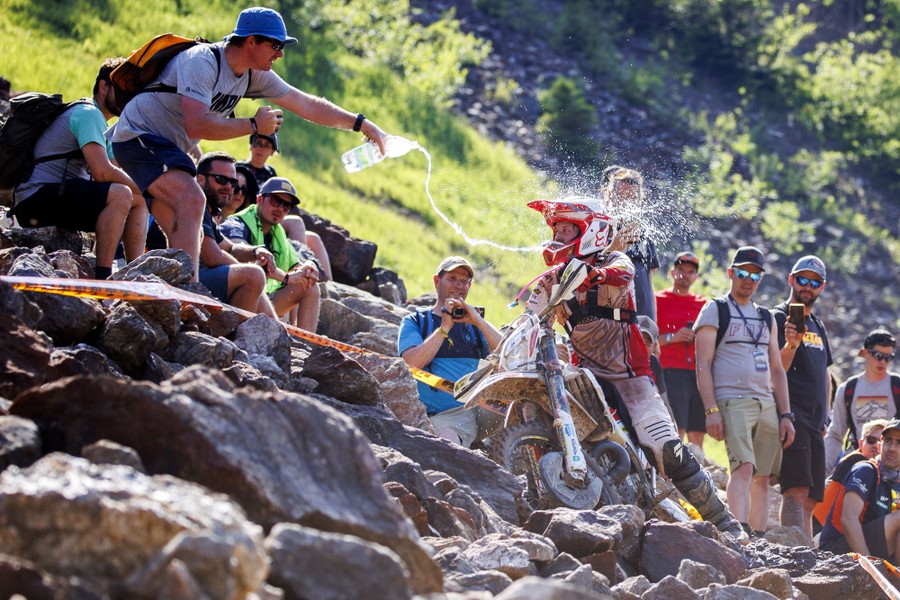A spectator splashes water from a bottle onto a motorcycle rider as he passes.