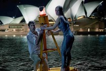 a man and a woman cling to a buoy in the ocean in front of the sydney opera house