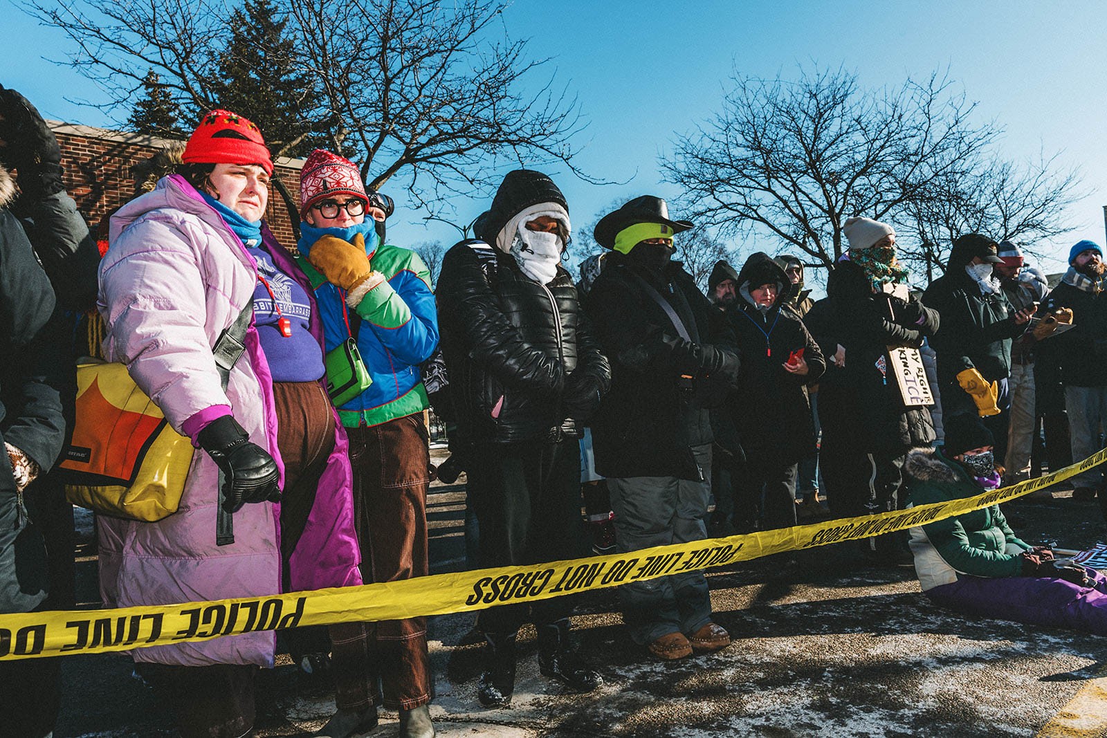 A crowd of people stand in front of police tape