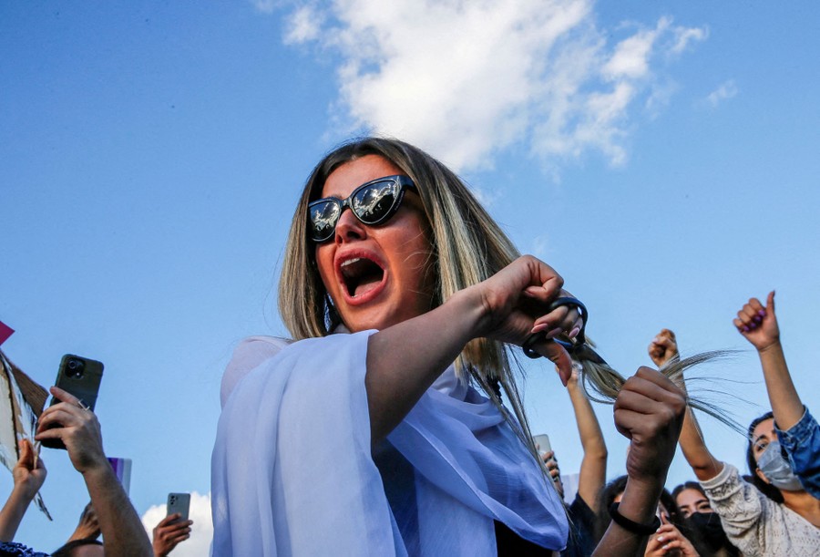 A protester cuts her long hair as others cheer nearby.