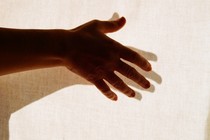a hand outstretched in front of a white curtain, its shadow beneath it