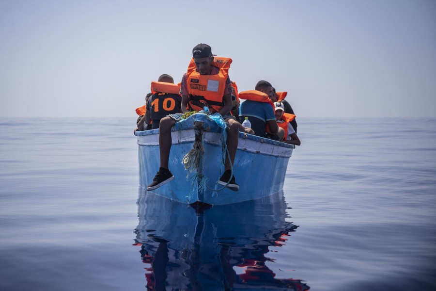Several people wearing life vests sit aboard a small boat in the open ocean.