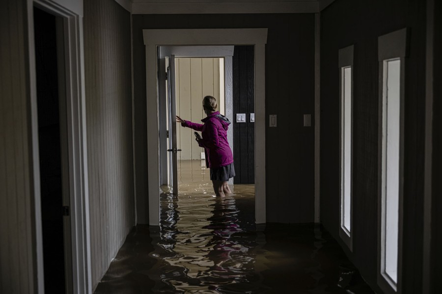 A person walks through a home, standing knee-deep in floodwater.