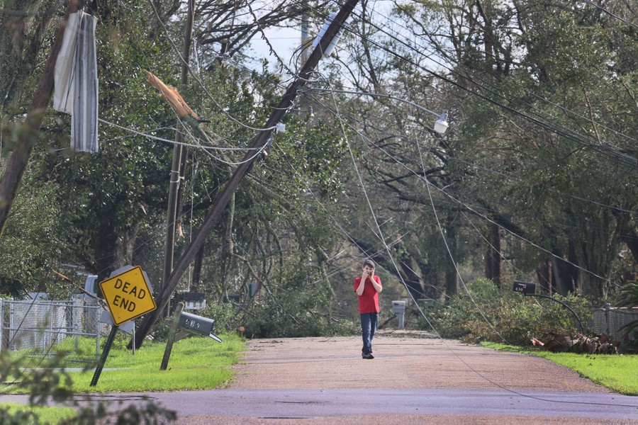 A person walks down a residential street with fallen trees and utility poles behind them.