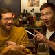 Billy Eichner and Luke Macfarlane laughing at a dinner table in "Bros"