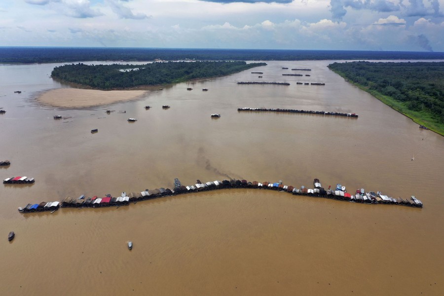Hundreds of barges float in lines in the middle of a large river.