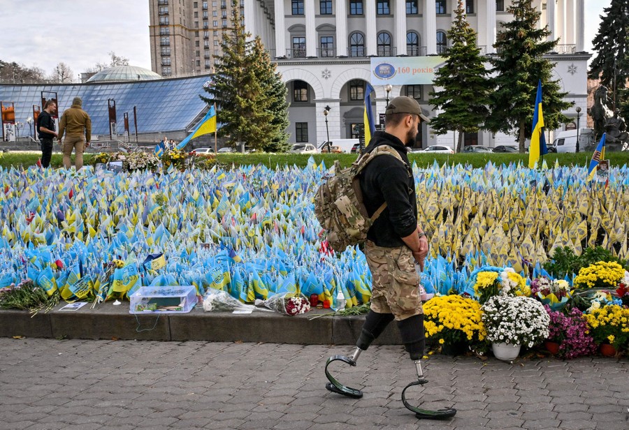 A serviceman wearing prosthetic legs walks past hundreds of small Ukrainian flags in a park.