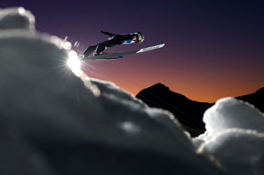 A ski jumper mid-jump, with clumps of snow in the foreground