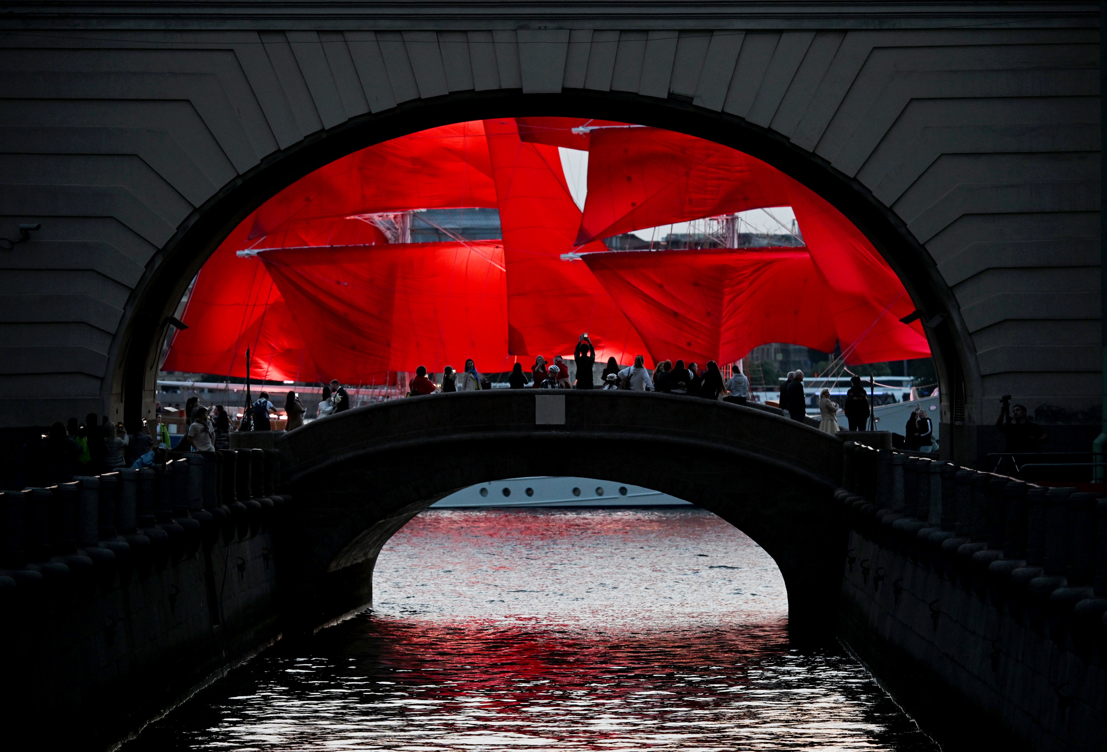A tall sailing ship with red sails passes by an archway.