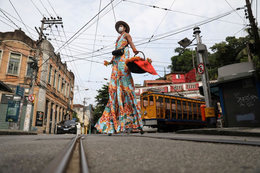 A person on stilts, wearing a long, flowing costume, walks in a city street near a trolley.