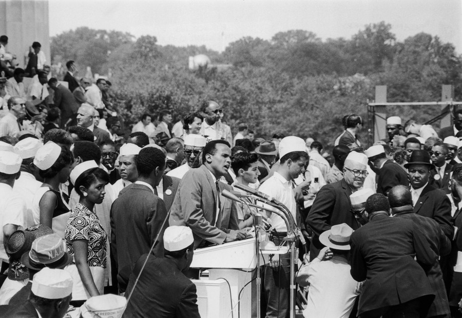 Part of a large crowd at the Lincoln Memorial, around Harry Belafonte, who speaks at a bank of microphones.