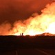 A red sky and yellow-lit smoke background USGS scientists working in front of the actively outgassing Fissure 8 vent, in Hawaii.