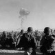 A group of troops watch a plume of smoke rise in the sky.