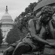 Black-and-white photo of a statue near the U.S. Capitol, whose rotunda is seen between trees in the background.