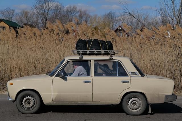 car packed with people driving with a field behind it.