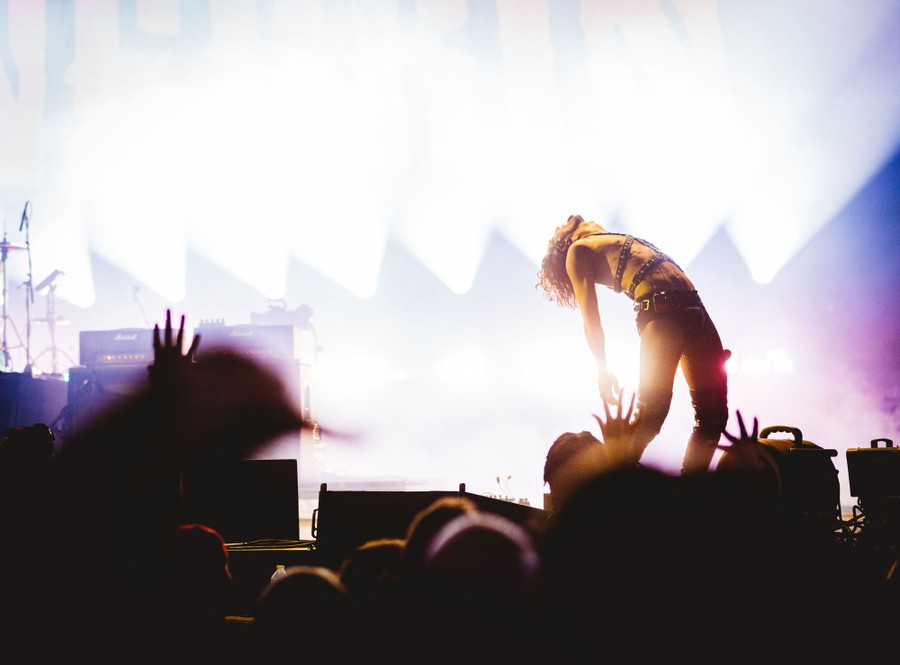 A performer strikes a pose onstage, beyond the heads and outstretched hands of the audience.