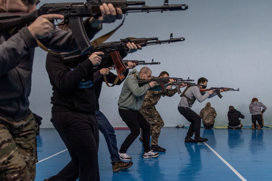 A half-dozen people train with rifles inside a gymnasium.