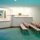 Three rows of chairs sit facing the head of a room in a funeral home. On one chair is a box of tissues.